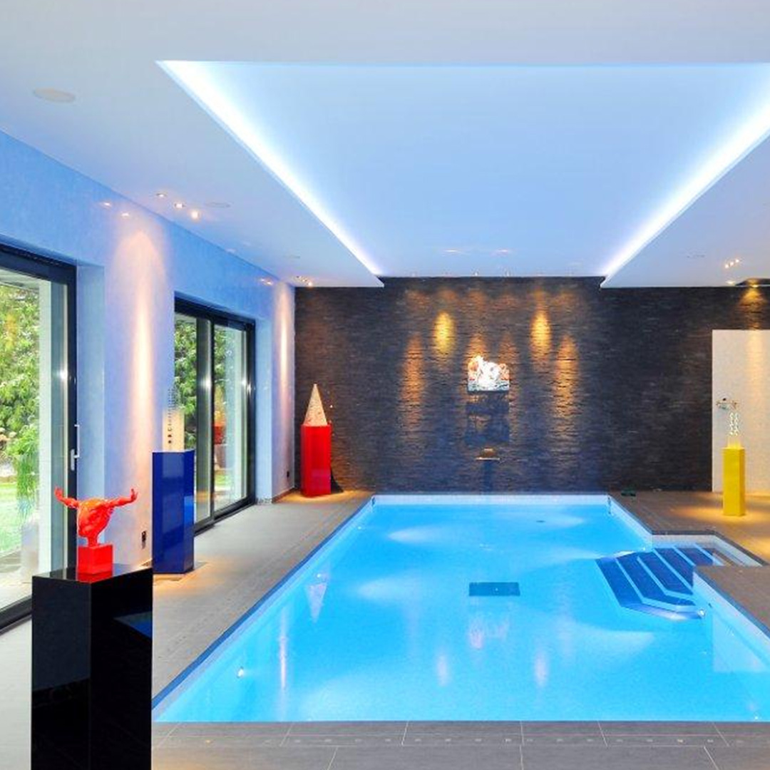 Ein moderner Innenpool mit blauer Beleuchtung und farbigen Skulpturen in einem luxuriösen Raum.