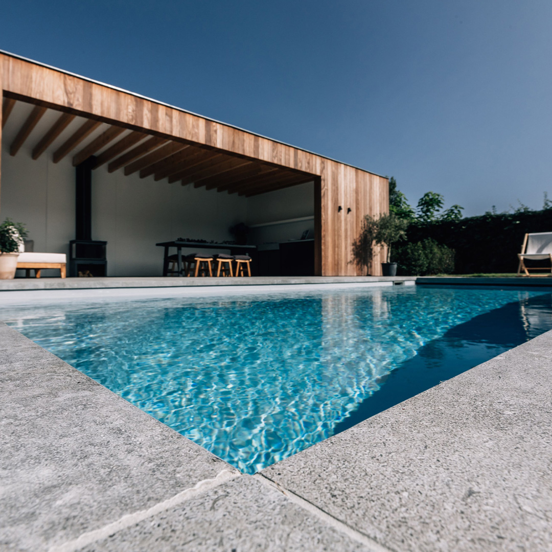 Moderner Pool mit Holzveranda, blauer Himmel, klare Wasseroberfläche und Holzmöbeln.