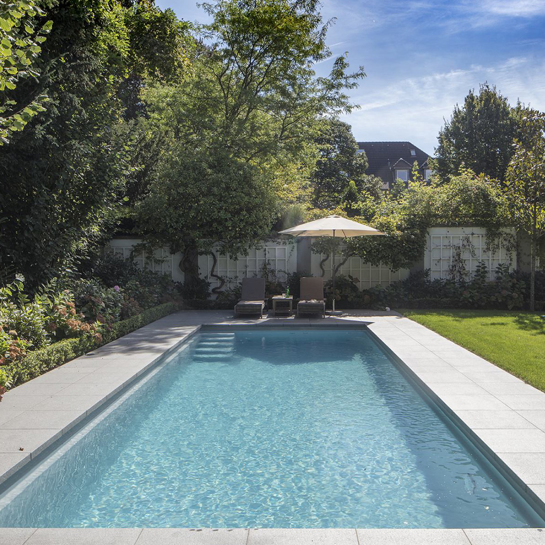 Ein eleganter Garten mit Schwimmbad, zwei Liegen und Sonnenschirm. Entspannte Atmosphäre.