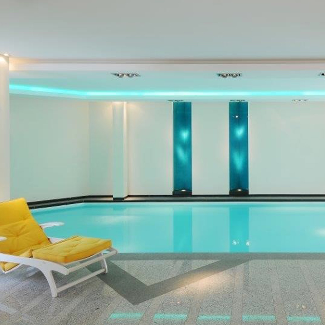 Innenpool, türkis beleuchtet, mit gelben Liegen und moderner eleganter Gestaltung.