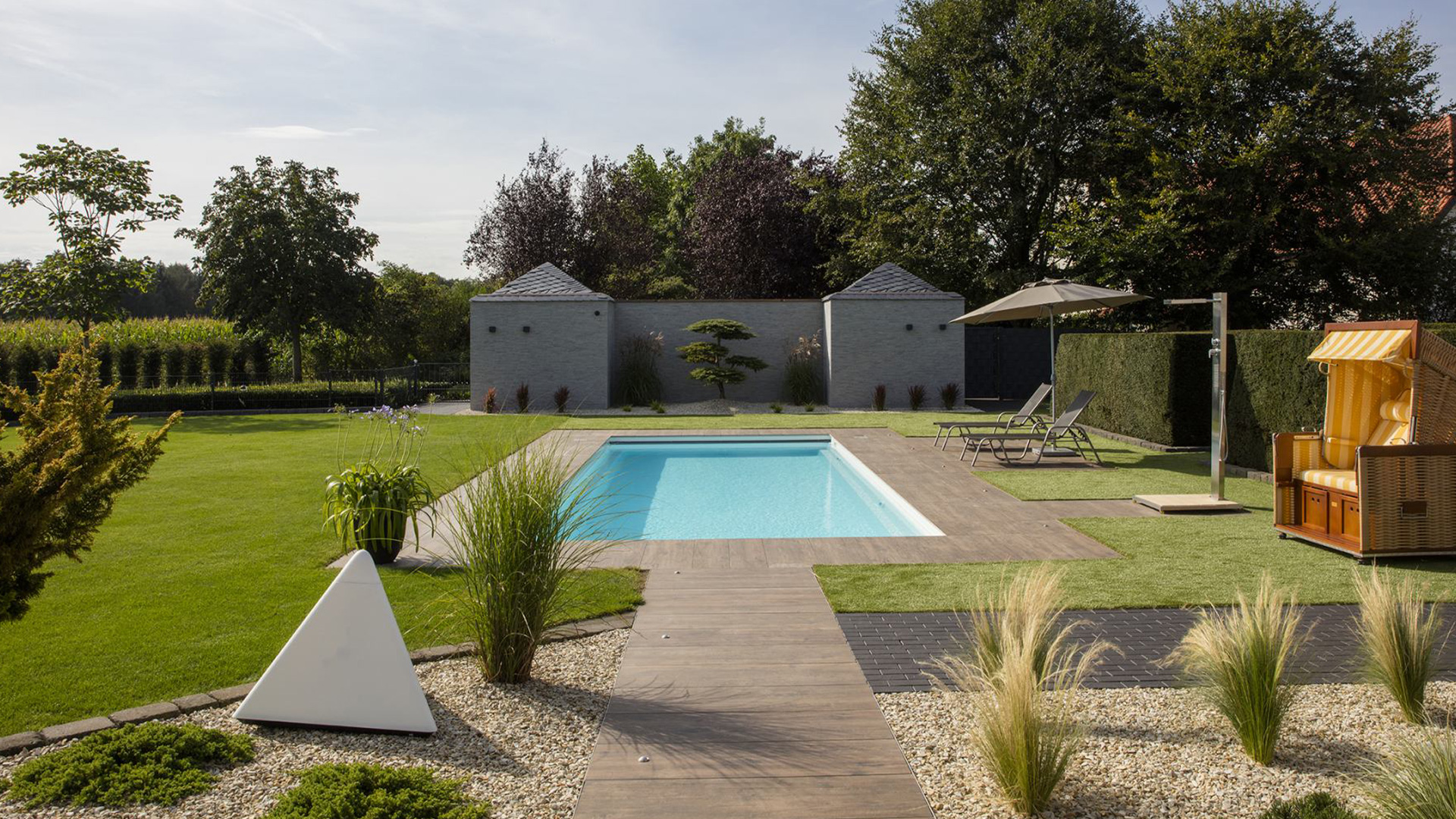 Ein moderner Garten mit Pool, Holzweg, Liegestühlen, Sonnenschirm und gepflegtem Rasen.