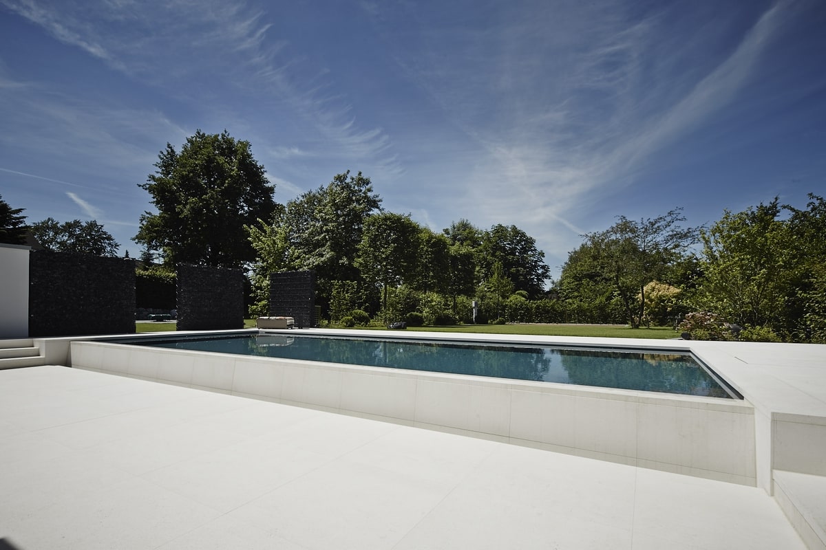 Ein leerer Pool in modernem Garten, umgeben von Bäumen und strahlend blauem Himmel.