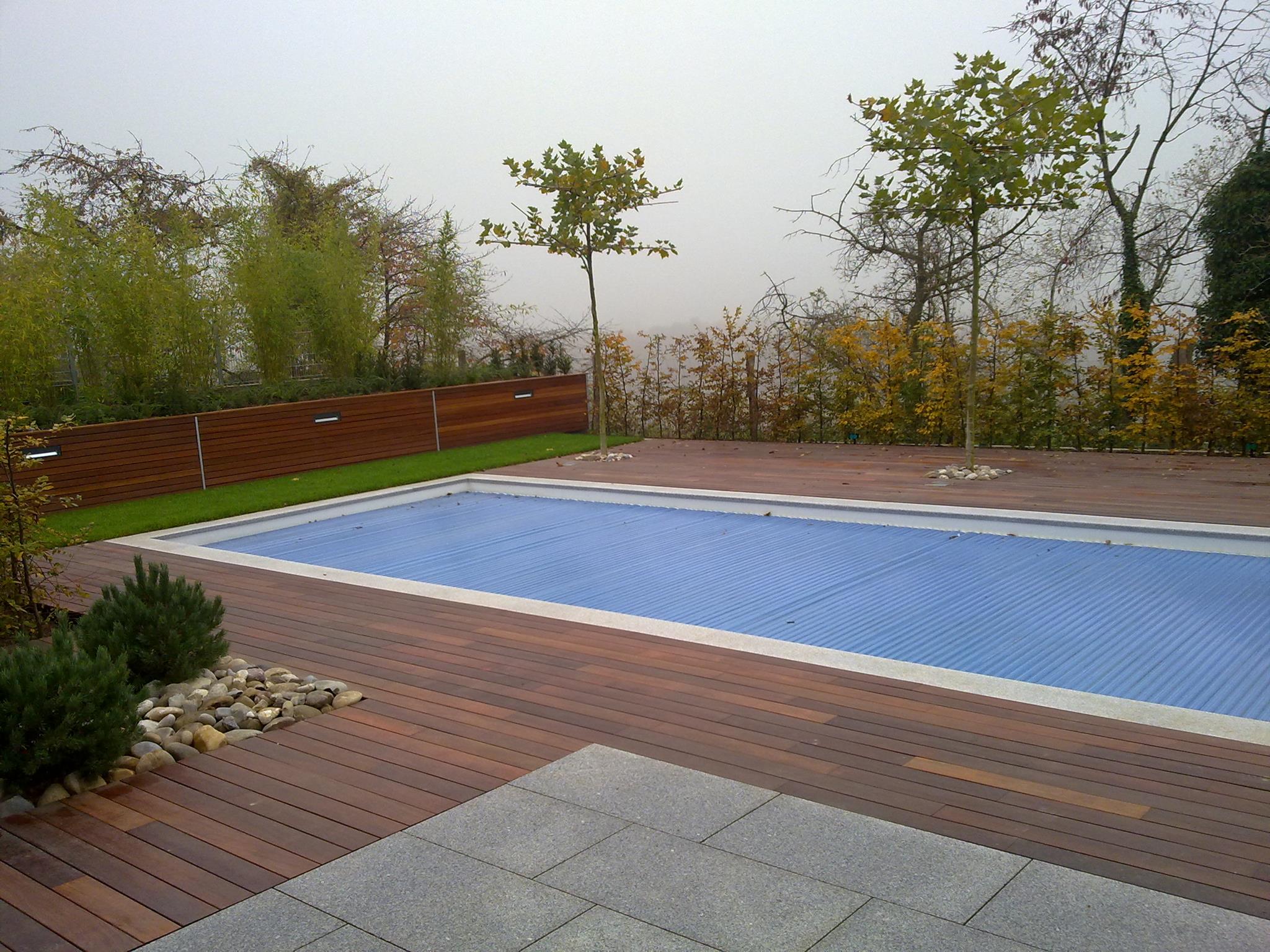 Ein leerer Pool mit blauer Abdeckung, umgeben von Holz und kahlen Bäumen im Hintergrund.