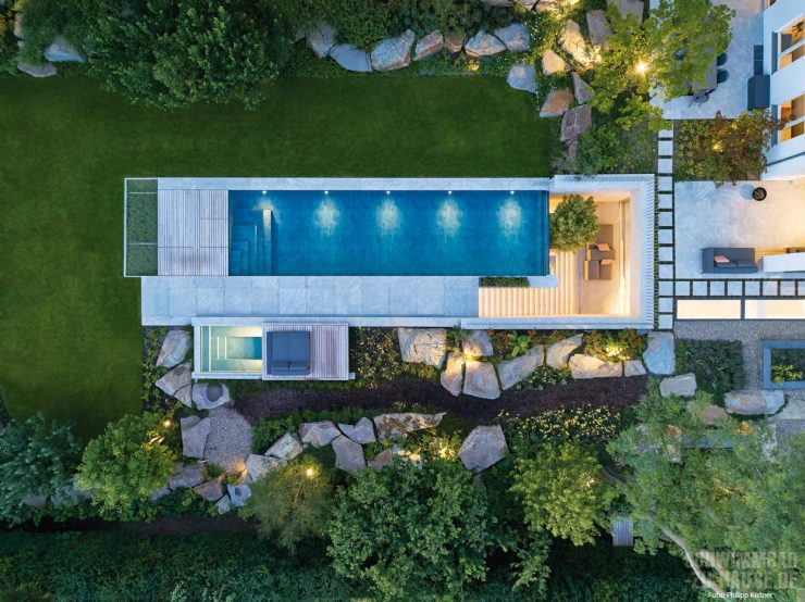 Luftaufnahme eines modernen Gartens mit Pool, grüner Rasen, Felsen und Bäumen bei Nacht.
