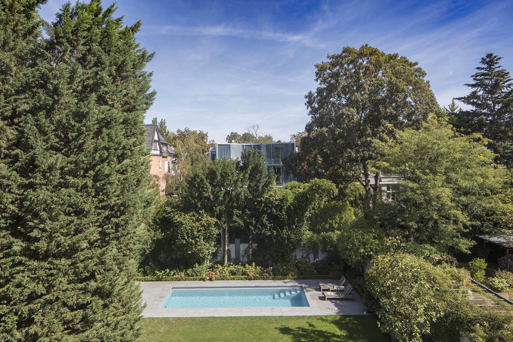Ein gepflegter Garten mit großem Pool, umgeben von Bäumen, unter blauem Himmel.