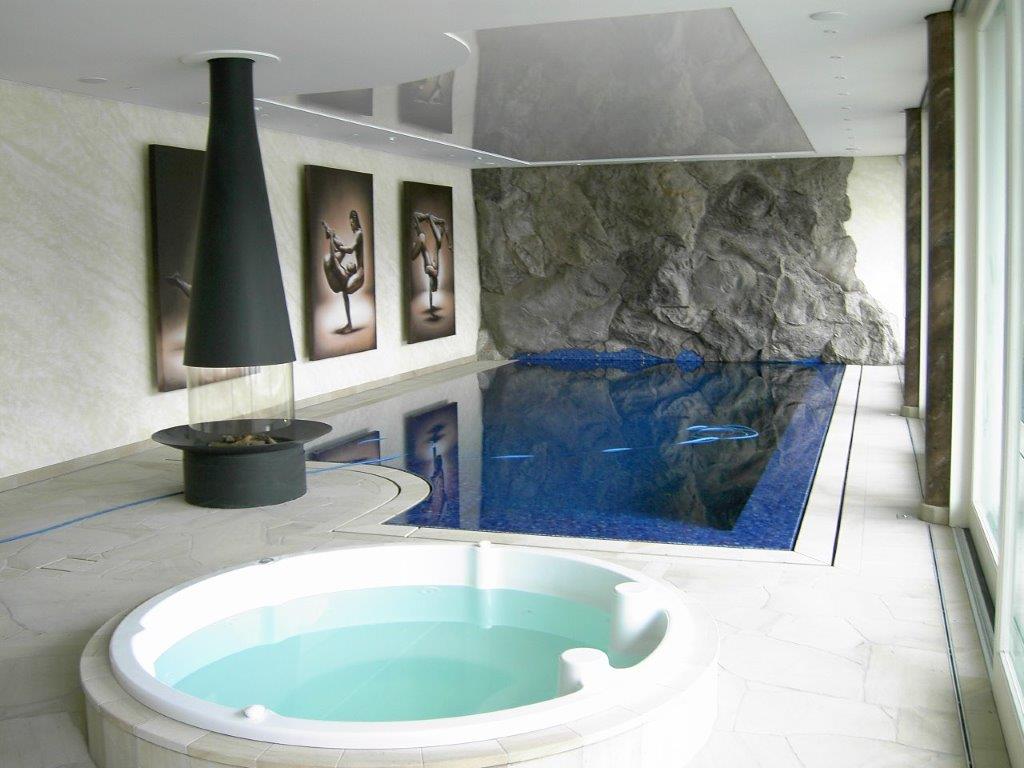 Innenpool mit blauen Fliesen, Natursteinwand, Kunstwerken, Kamin und Whirlwanne in elegantem Raum.
