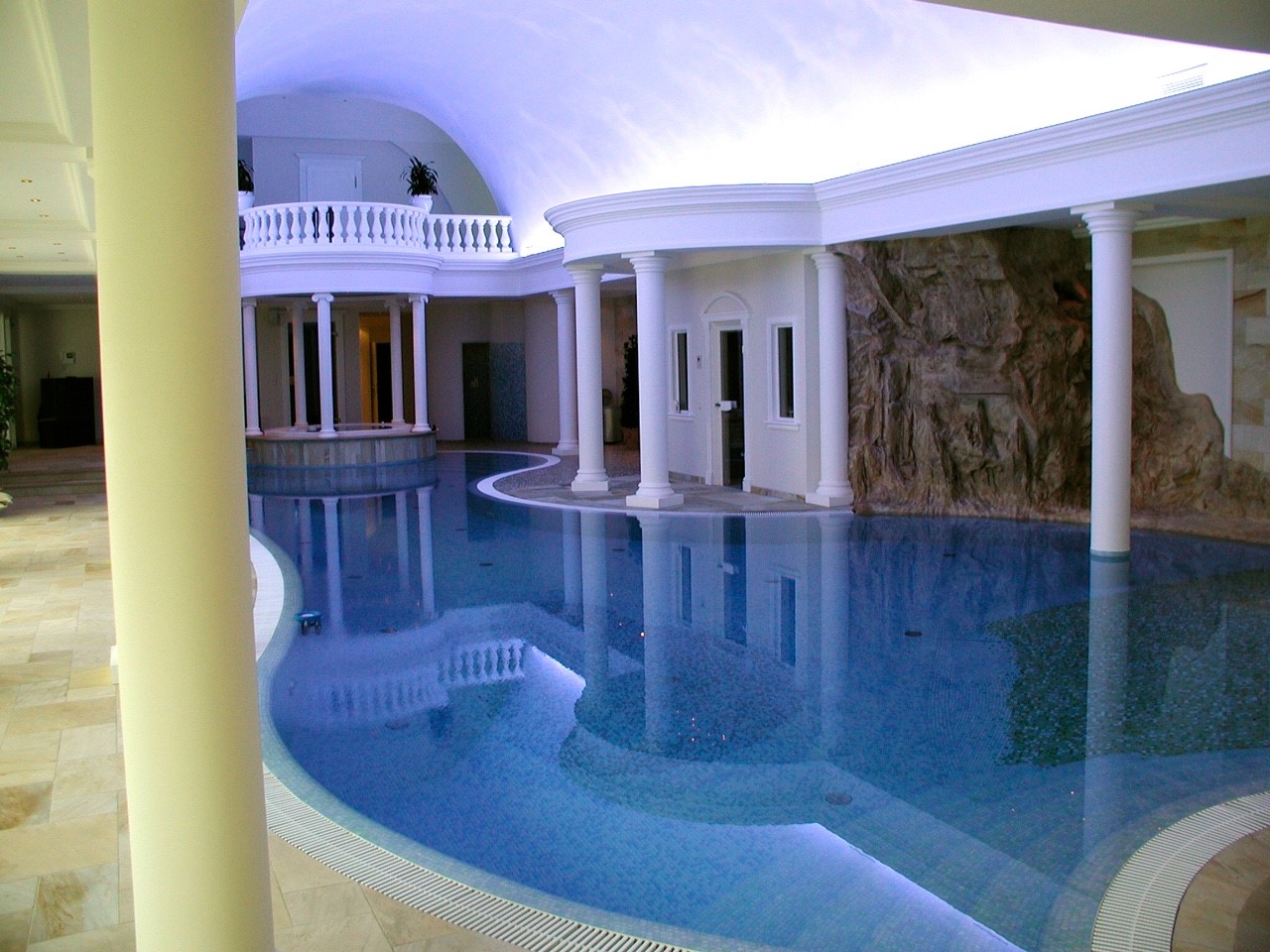 Innenpool mit Säulen, edlem Marmor, natürlicher Felswand und eleganter, gewölbter Decke.