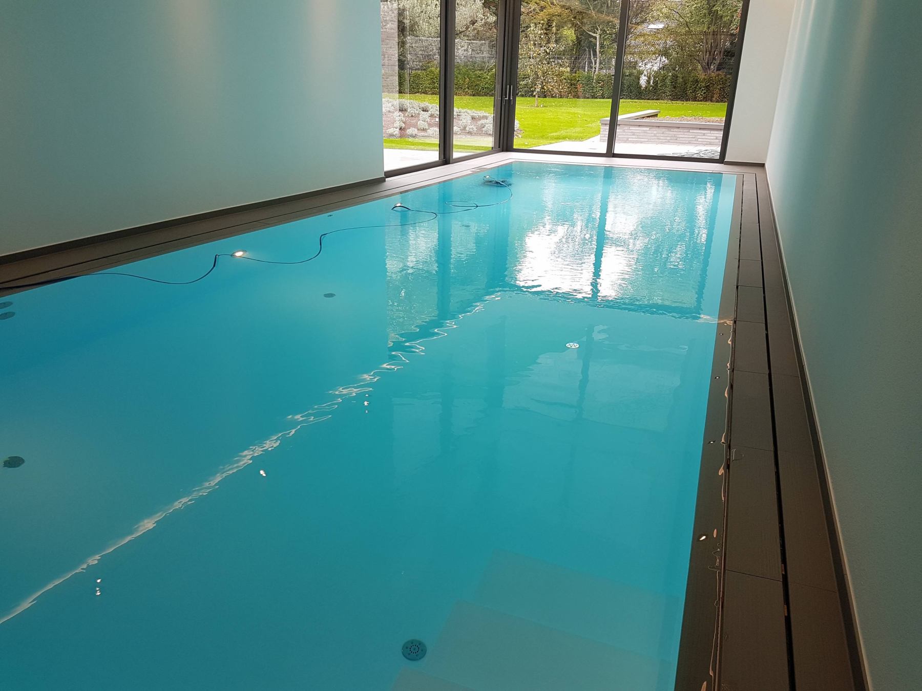 Innenpool mit glattem, blauem Wasser, umgeben von hellen Wänden und großen Glasfenstern.