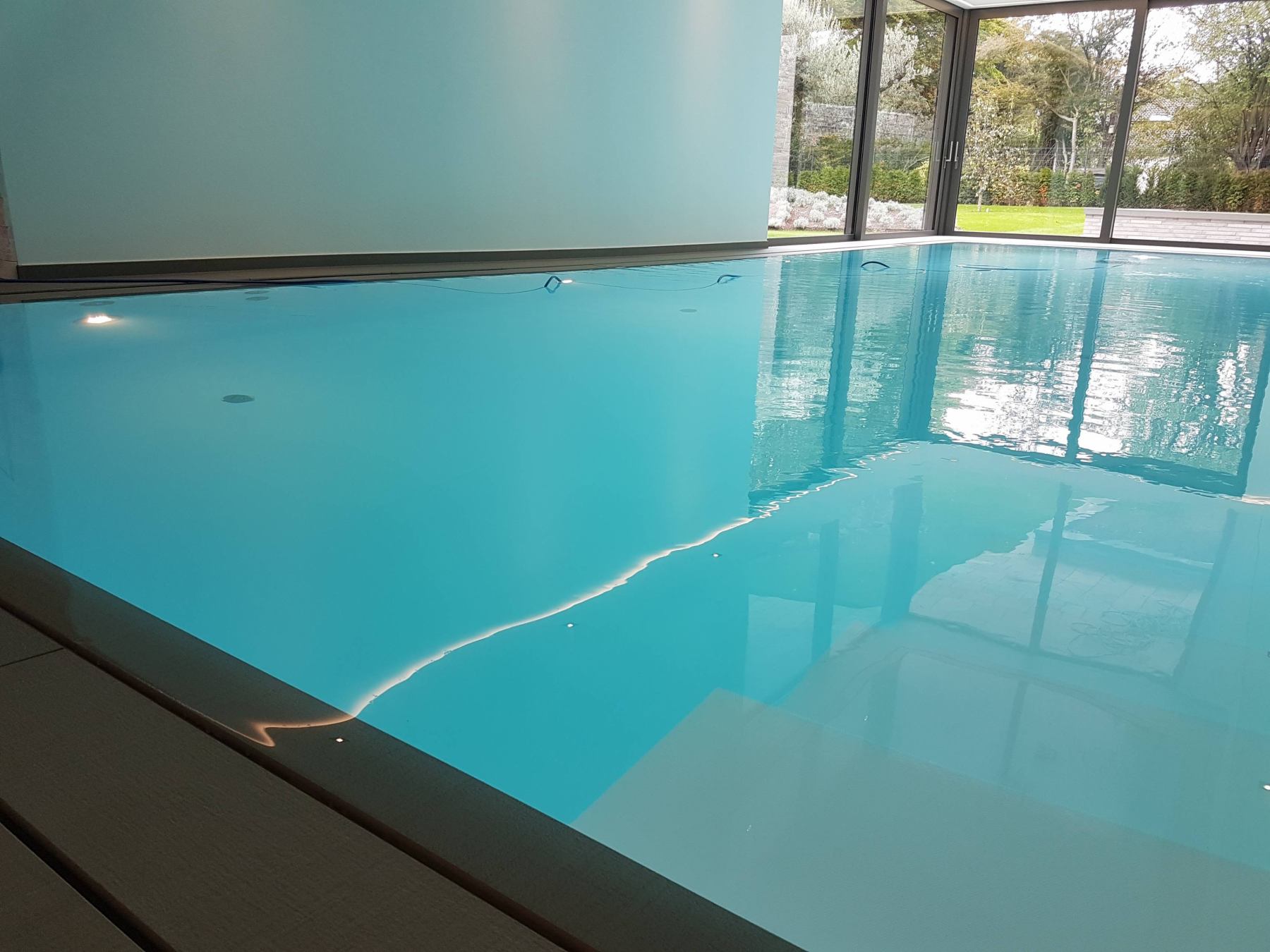 Innenpool mit ruhigem, klarem Wasser, umgeben von großen Fenstern mit Blick auf einen Garten.