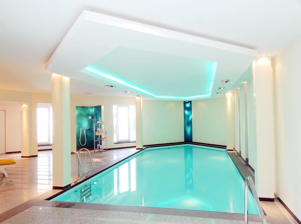 Großer Innenpool mit hellblauem Wasser, modernen Deckenlichtern und eleganten Wandfarben.