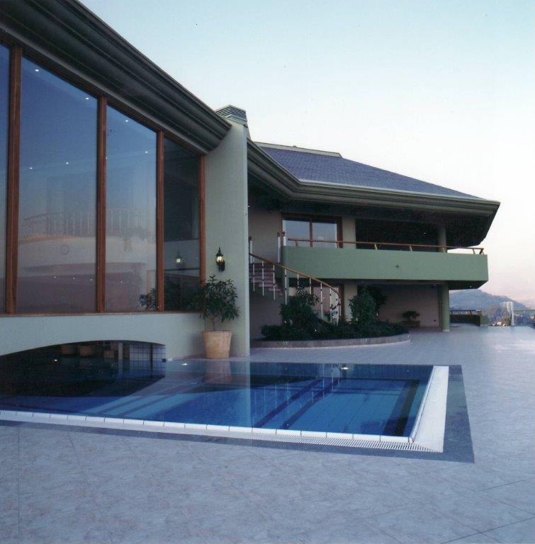 Außenansicht eines modernen Hauses mit Pool und großen Glasfenstern bei Tageslicht.