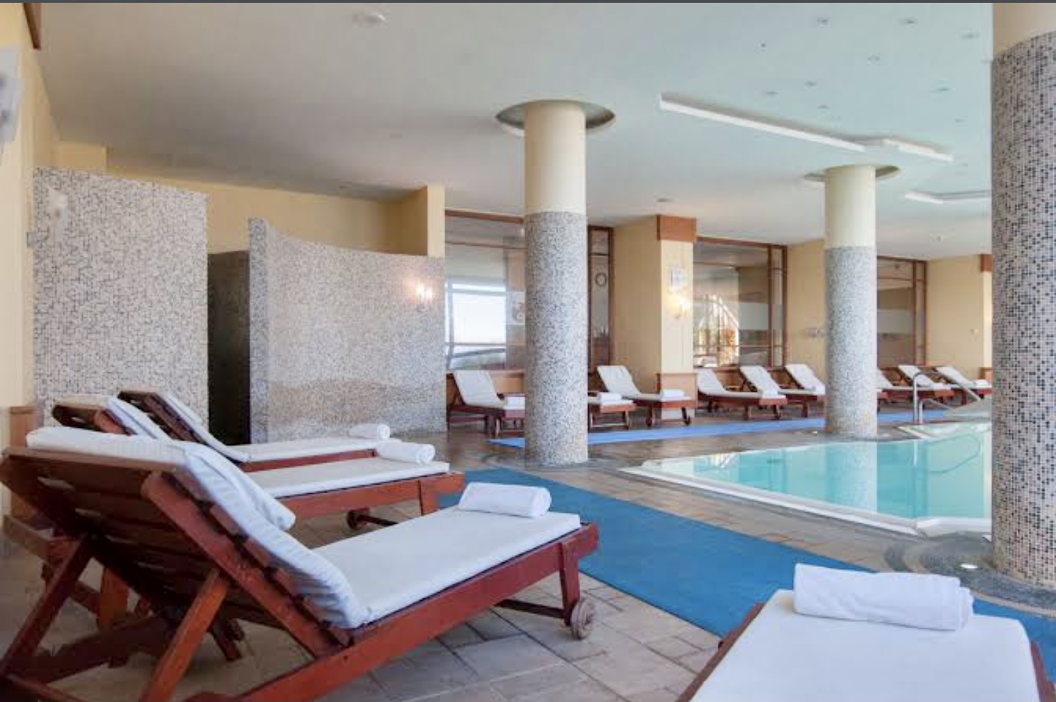 Innen-Poolbereich mit Liegestühlen, weiß-blauem Design und modernen Säulen.