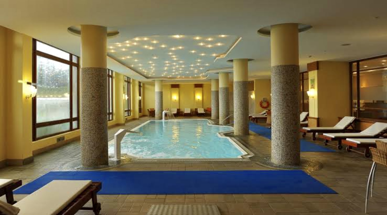 Innenpool mit Liegestühlen, gelben Wänden und Sternendeckenleuchten in einem Wellnessbereich.