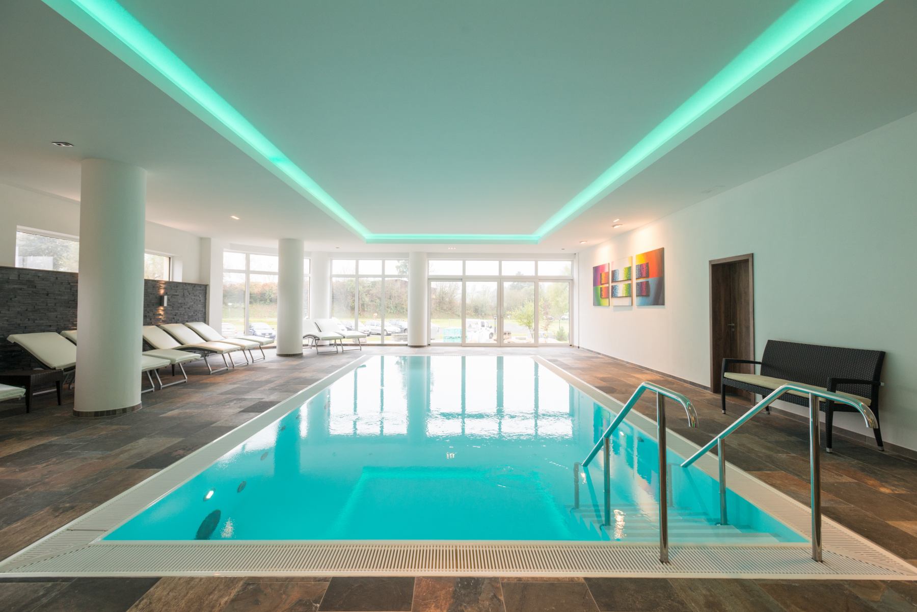 Innenpool mit Liegestühlen, großen Fenstern, abstrakten Kunstwerken und dezentem Licht.