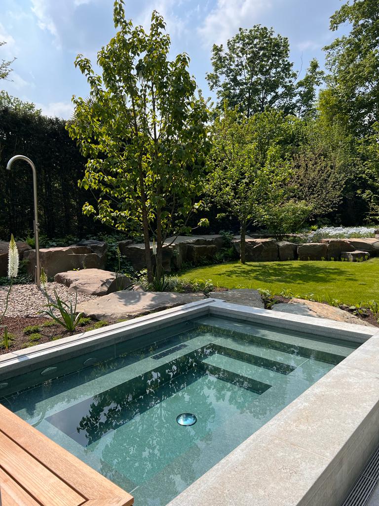 Gartenansicht mit kleinem Pool, Bäumen und grünem Rasen an einem sonnigen Tag.
