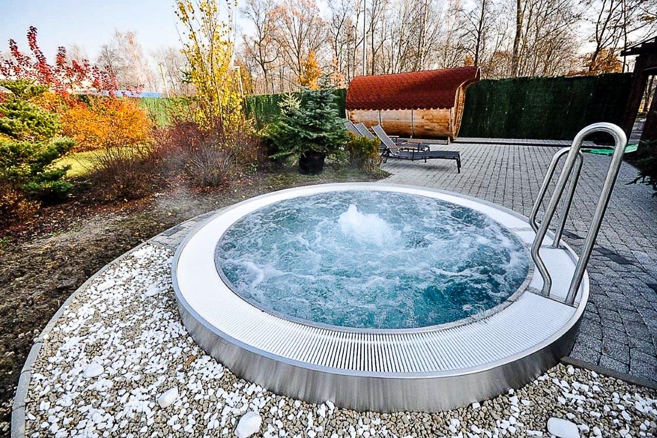 Ein sprudelnder Whirlpool im Freien, umgeben von Herbstbäumen und Kieselsteinen.