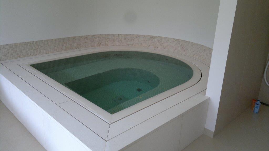 Ein leeres weißes Jacuzzi in einem schicken, modernen Badezimmer mit beige gefliestem Hintergrund.