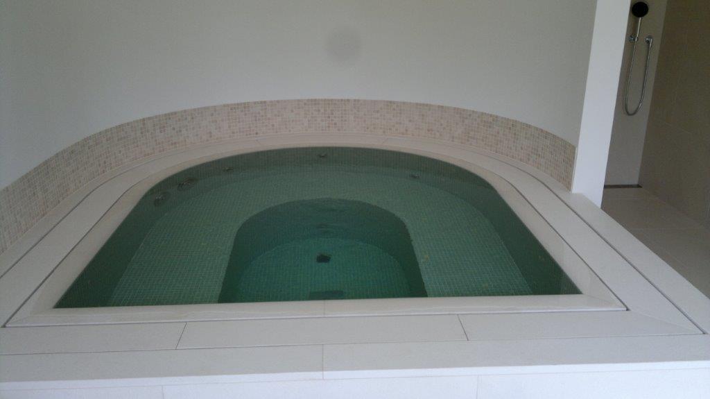 Ein leerer, moderner Whirlpool in einem hellen Raum mit Mosaikwandverkleidung im Hintergrund.