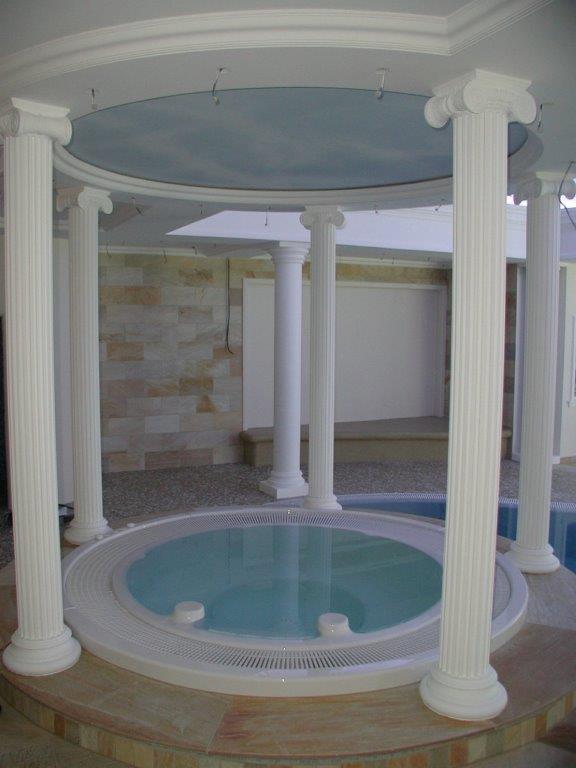 Weißer Rundpavillon mit Säulen um einen blauen Whirlpool in elegantem Innenbereich.