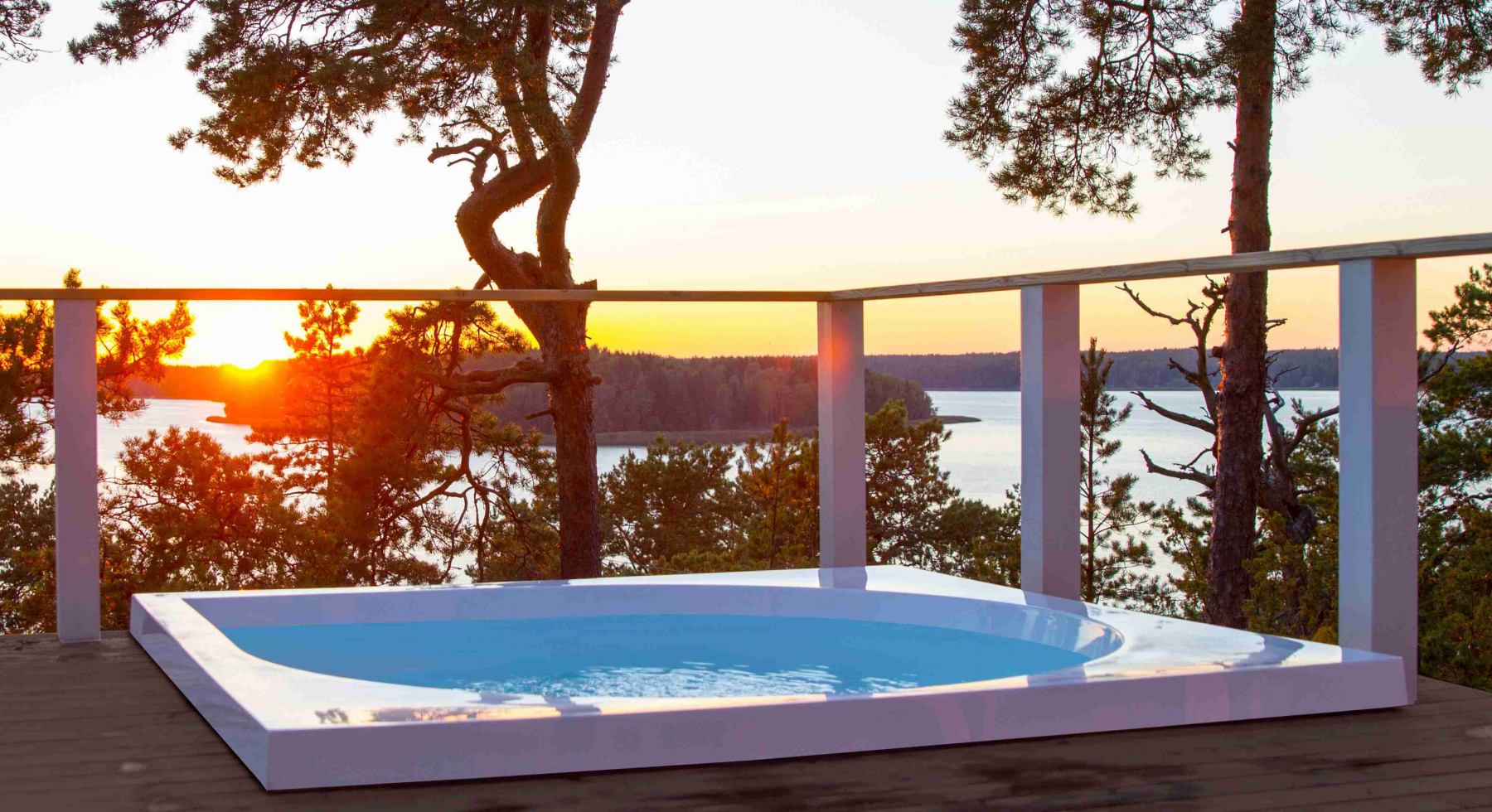 Sonnenuntergang über See hinter einem modernen weißen Whirlpool auf einer Terrasse.