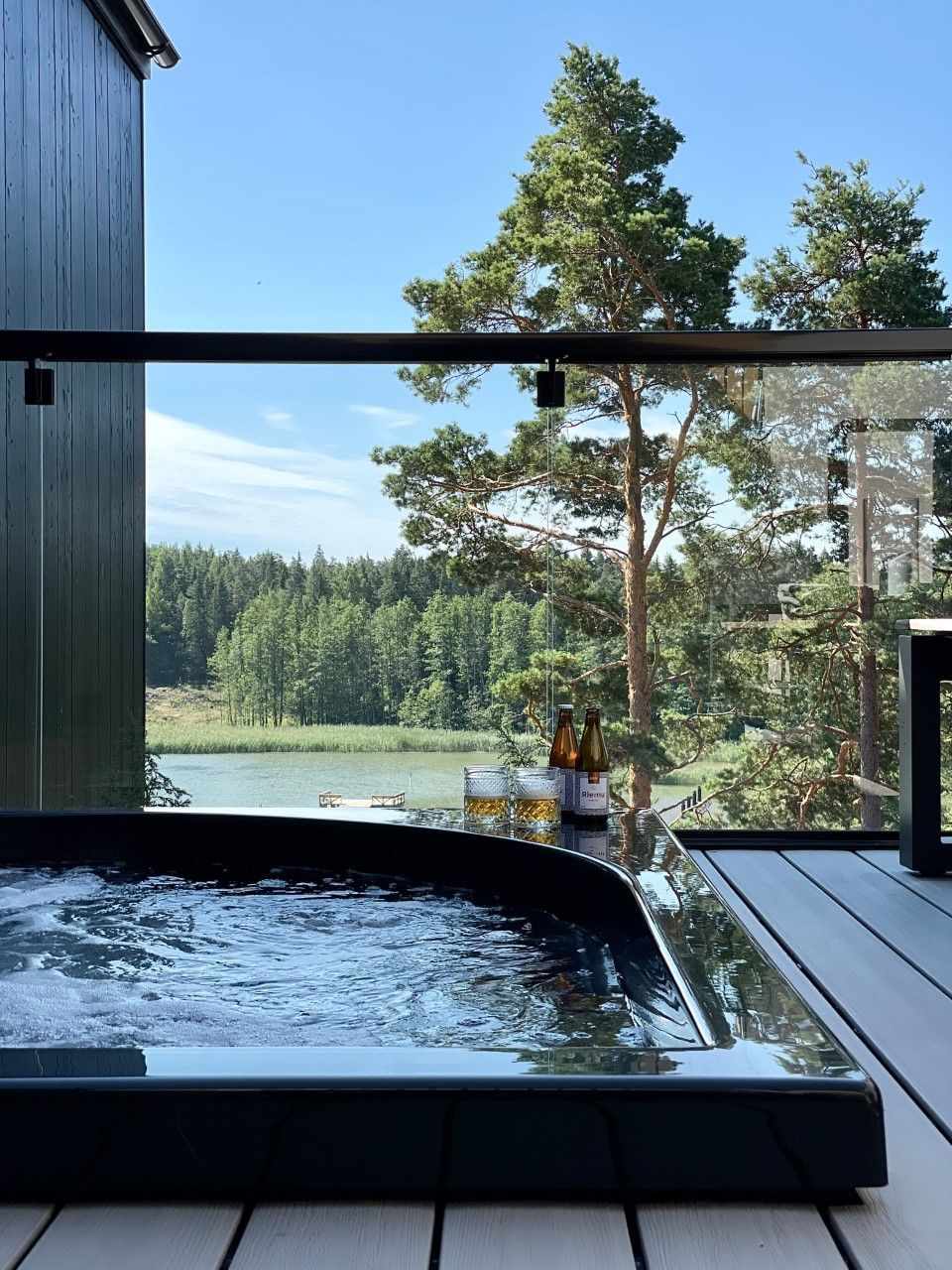 Whirlpool auf Terrasse, Blick auf Wald und See, Sonnenlicht, ruhige Atmosphäre.