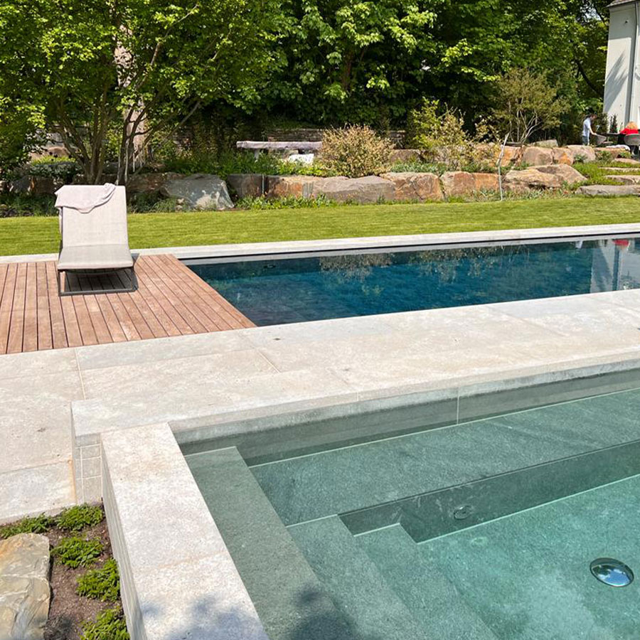 Poolbereich mit klarem Wasser, Holzliege und Garten im Hintergrund, sonnig und friedlich.