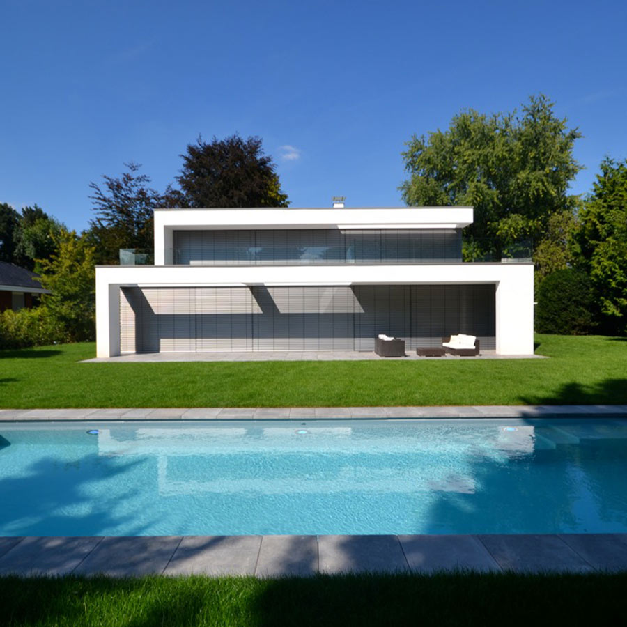 Ein minimalistisches, zweistöckiges, weißes Haus mit Pool im Vordergrund und Bäumen im Hintergrund.
