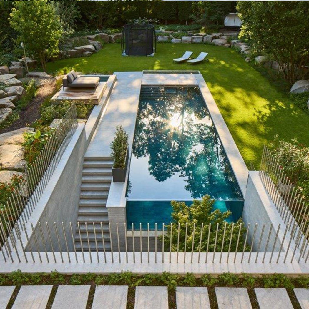 Rechteckiger Pool im Garten, umgeben von Steinen und Pflanzen, mit angrenzender Sitzfläche.