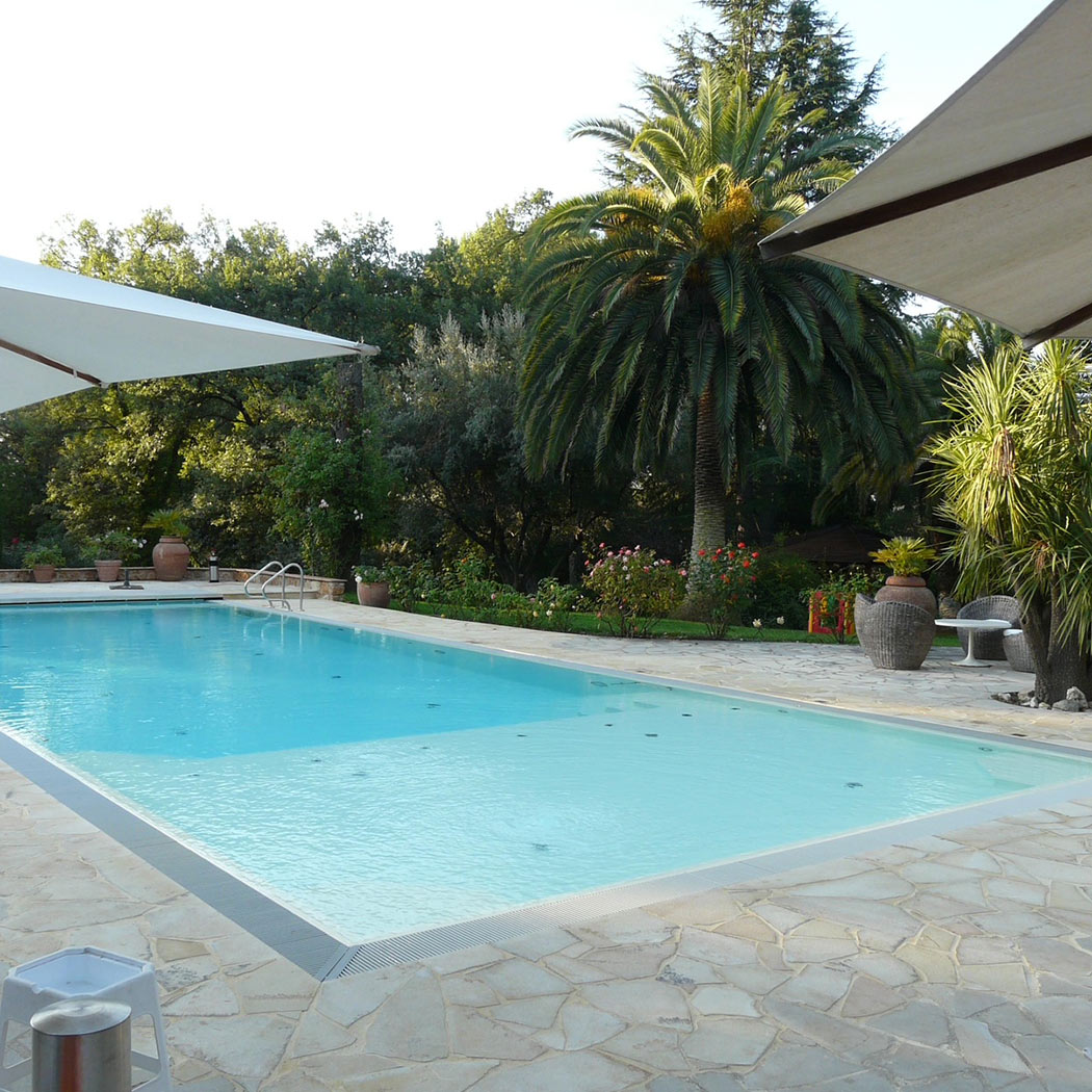 Ein ruhiger, von Palmen umgebener Pool am Tag mit sonnigem Himmel und grüner Landschaft.