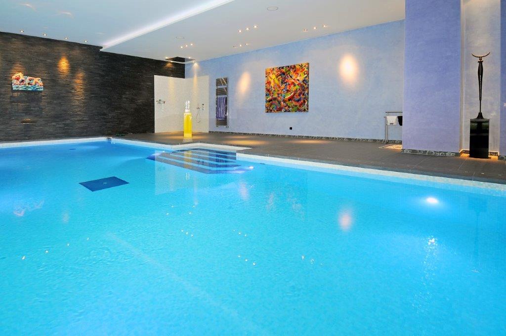 Innenpool mit hellblauem Wasser, bunter Kunst an der Wand, moderne Skulptur, elegante Beleuchtung.