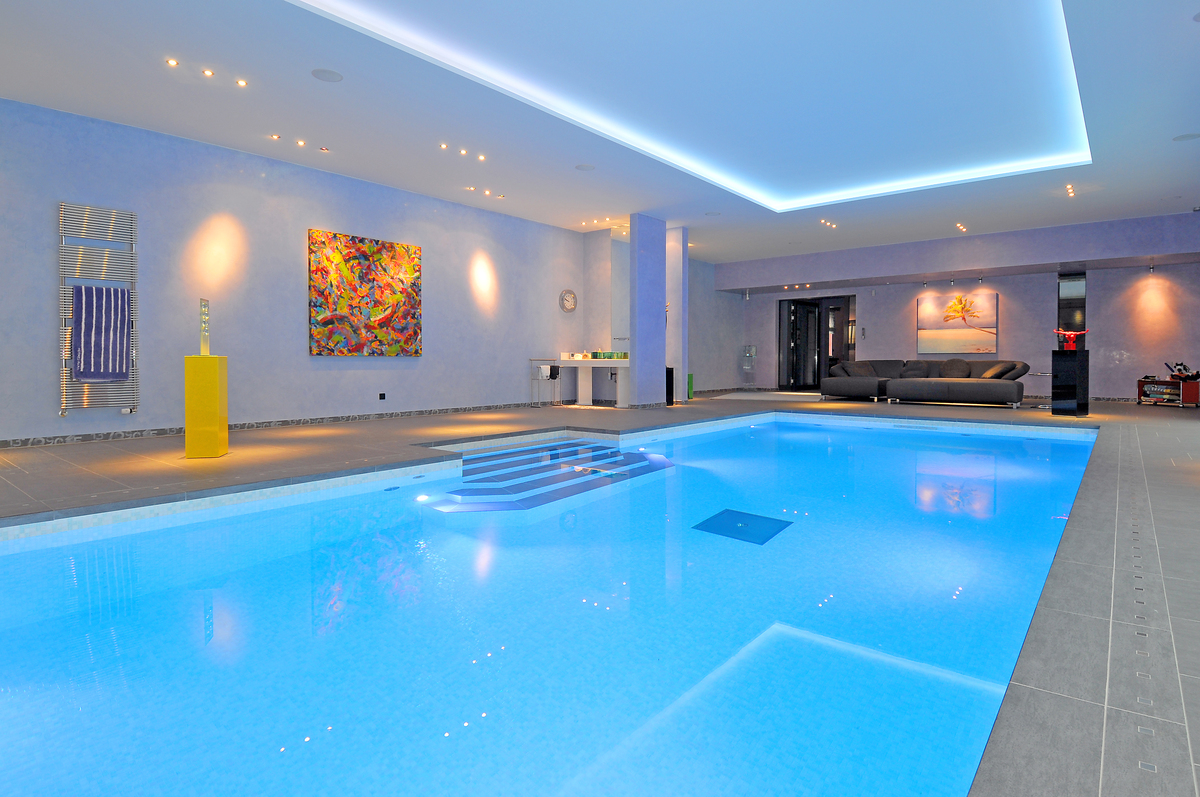 Beleuchtetes Hallenbad mit blauer Poolbeleuchtung, Kunstwerken an der Wand und moderner Einrichtung.
