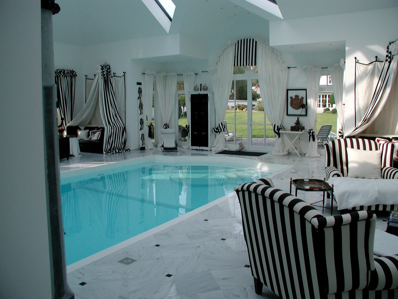 Ein eleganter Innenpoolbereich mit schwarz-weiß gestreiften Möbeln und großen Fenstern, Tageslicht.