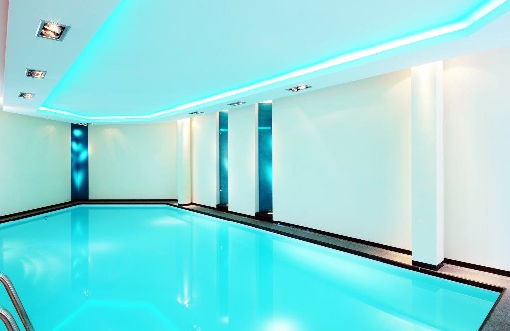 Innenpool mit heller Beleuchtung und klar blauem Wasser, umgeben von weißen Wänden.