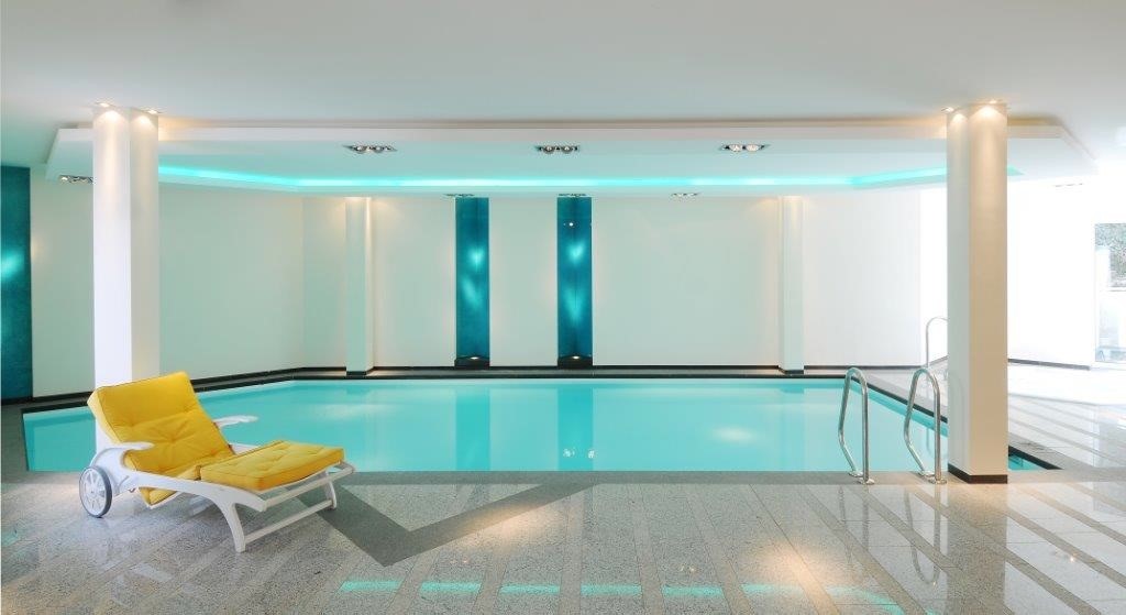 Hallenbad mit gelbem Liegestuhl, blauem Wasser und modernem, hellem Design.