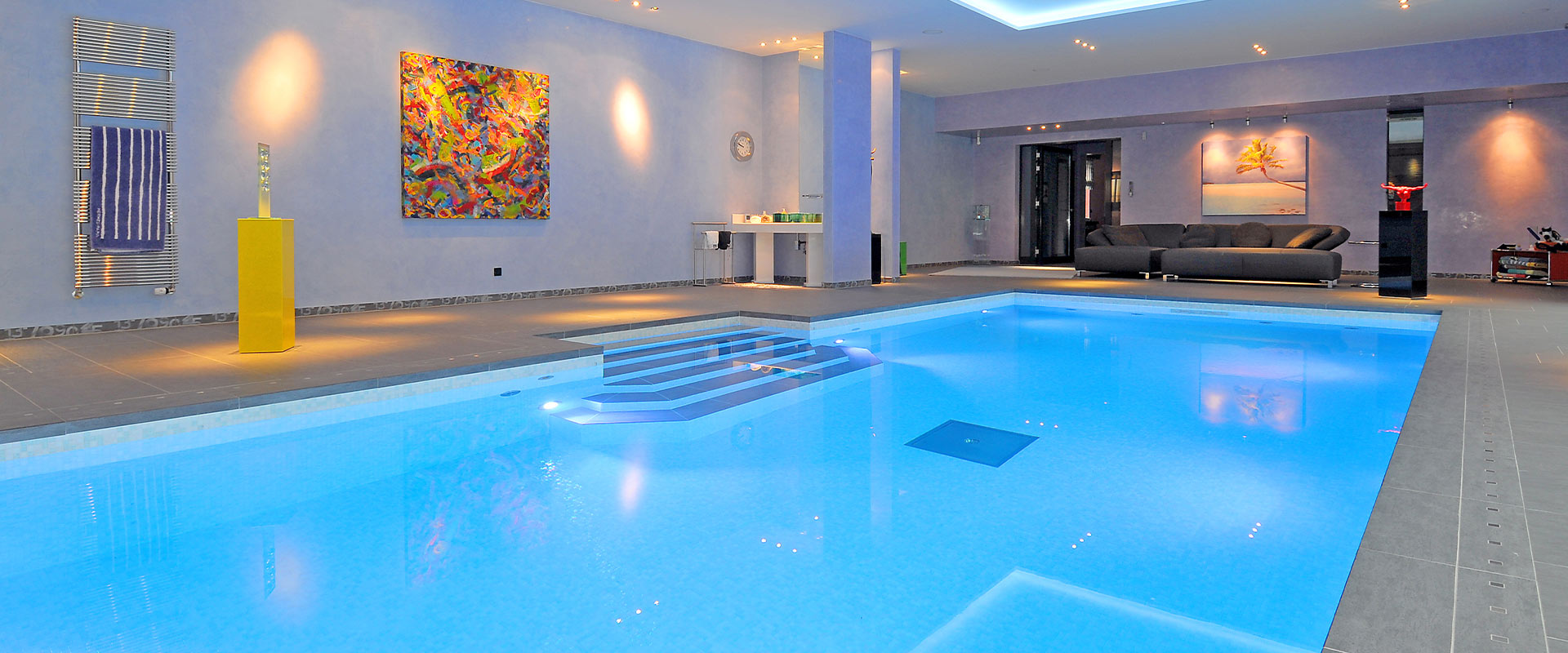 Luxuriöser Innenpoolbereich mit blauen Wänden, moderner Kunst und stilvoller Beleuchtung.