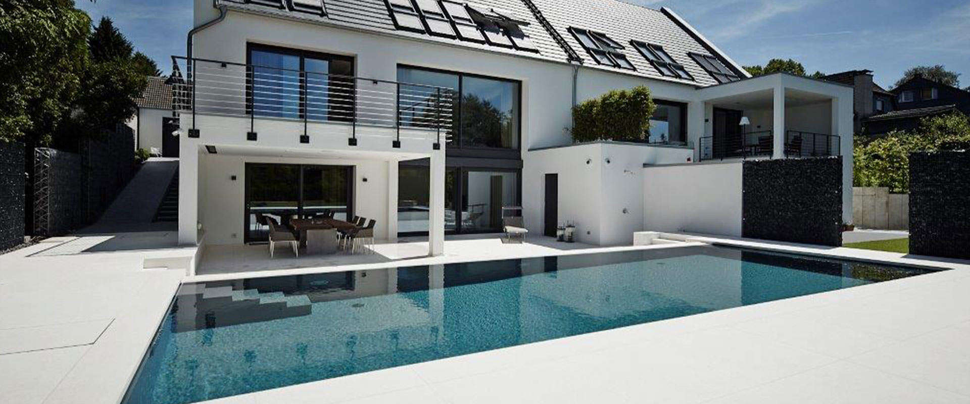 Modernes Haus mit großen Glasfenstern, weißer Fassade und einem Pool im Vordergrund.