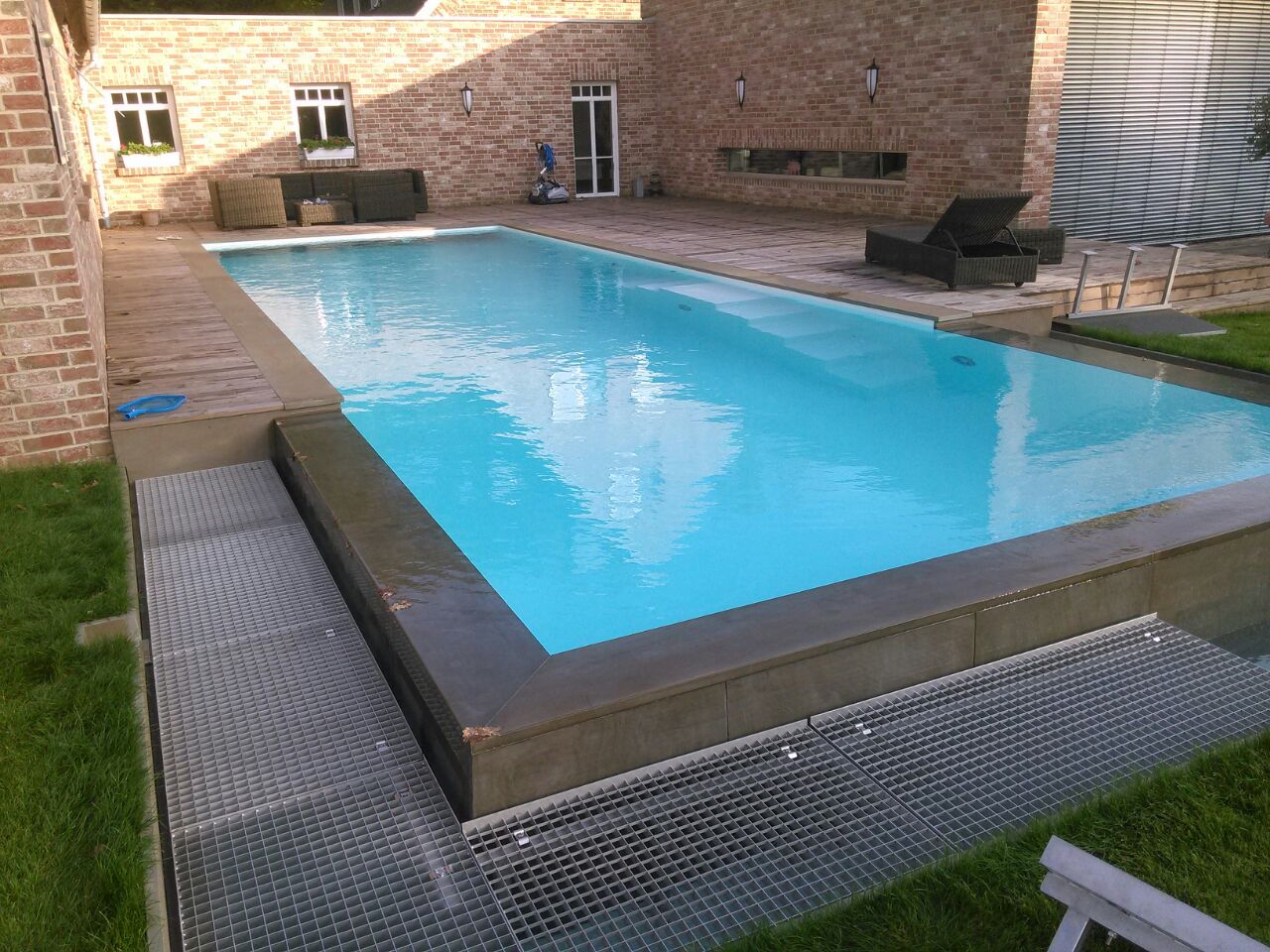 Ein moderner Außenpool mit klarem, blauem Wasser und Liegestühlen auf einer Holzterrasse.