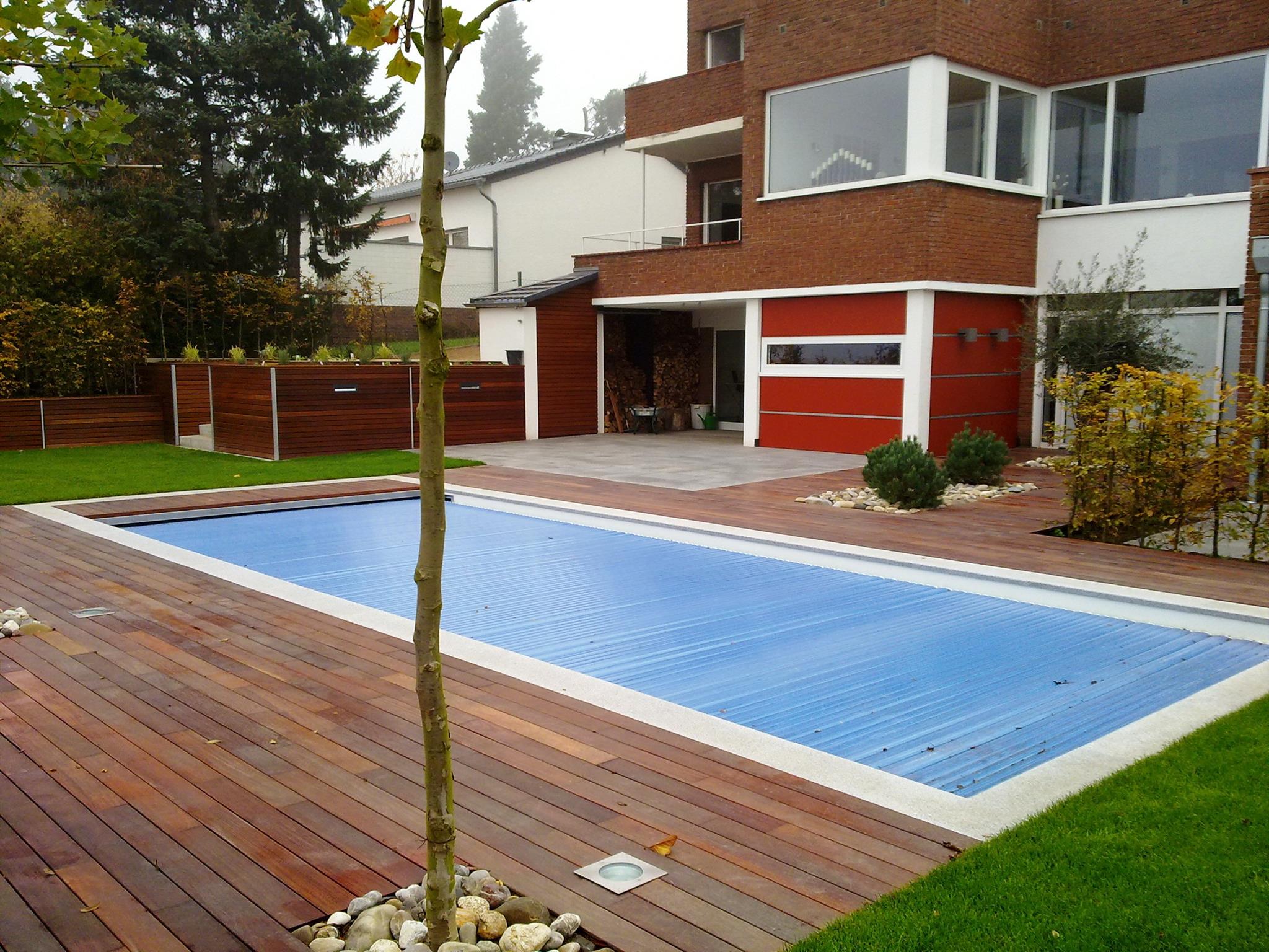 Ein moderner roter Backsteinhaus mit Holzdeck und abgedecktem Pool im Garten.