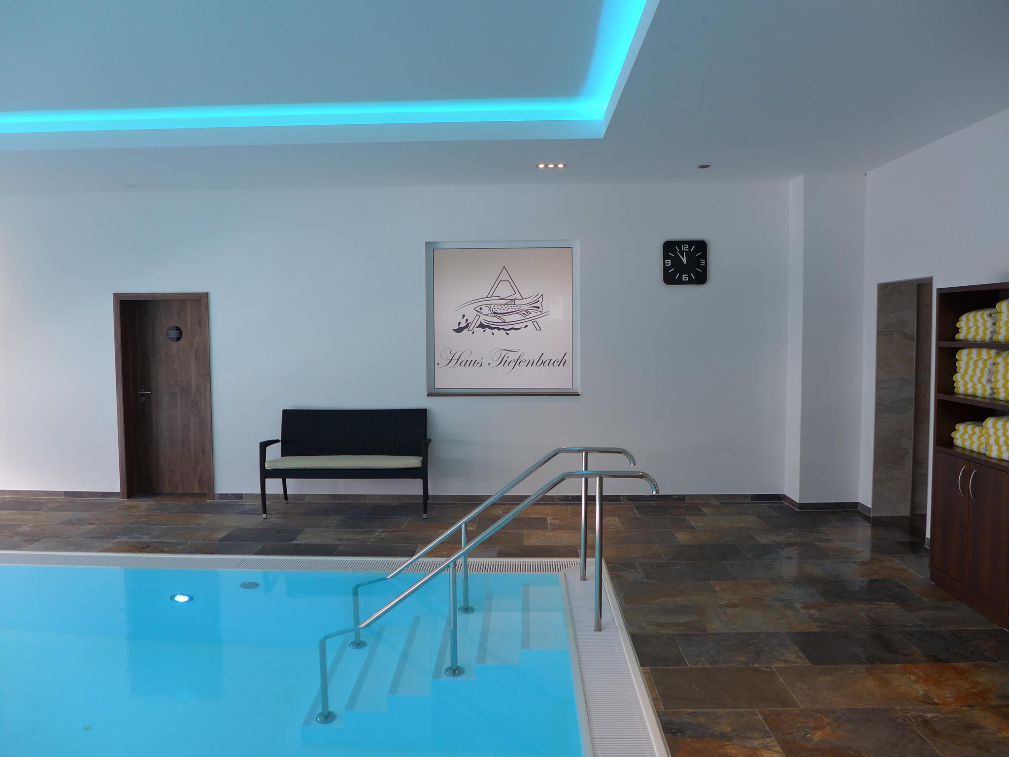 Innenpool mit blauem Wasser, Sitzbank, Uhr, Handtuchregal und einem Wandbild.