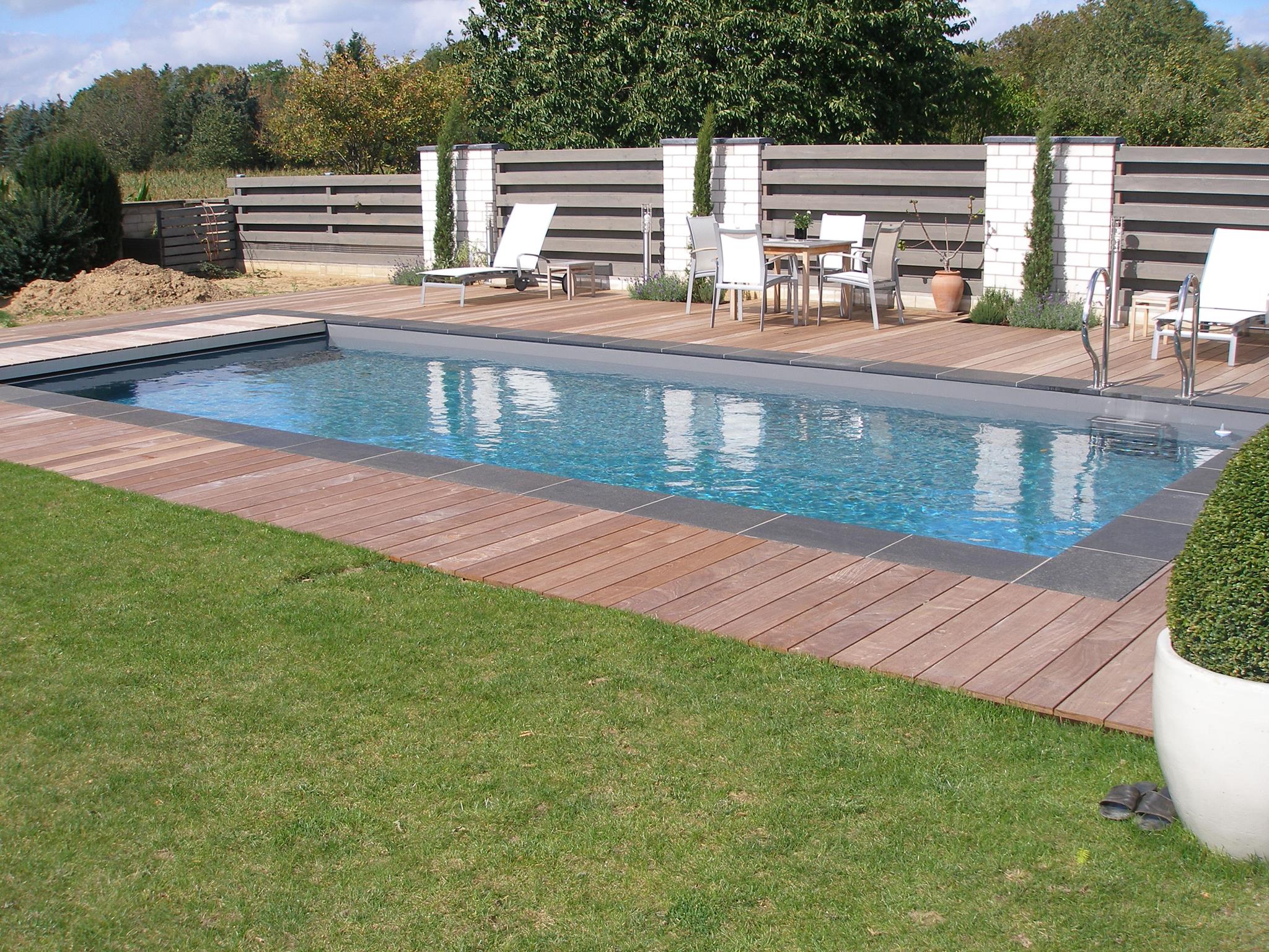 Ein moderner Gartenpool mit Holzdeck, umgeben von weißen Möbeln und Pflanzen.