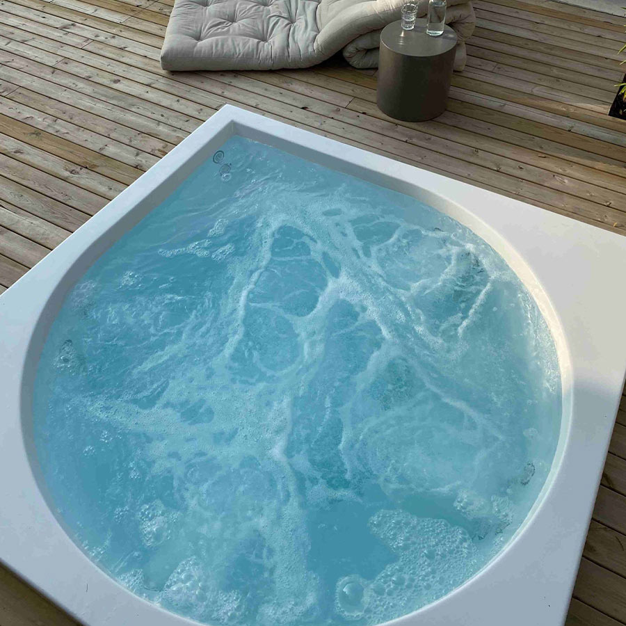 Whirlpool mit sprudelndem Wasser und mehreren Kissen auf einer Holzterrasse.