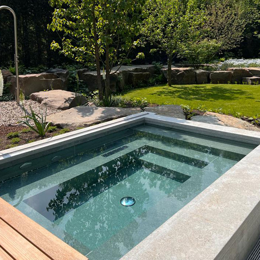 Rechteckiger, moderner Pool im Garten mit klaren, blauen Wasser; umgeben von Bäumen und Steinen.