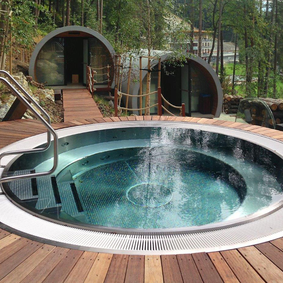 Rundes Außen-Whirlpool mit Stufen, umgeben von Holzdeck und moderner Waldunterkunft.