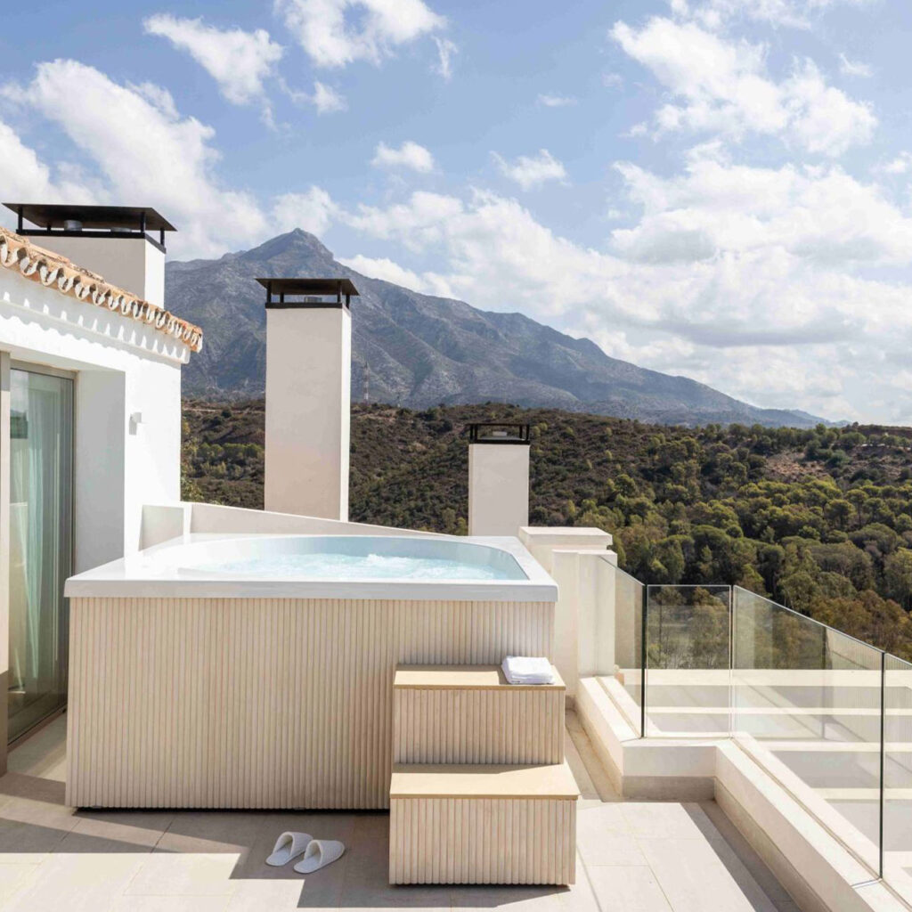 Whirlpool auf Terrasse mit Bergblick, leere Treppe, weiße Hausschuhe, klarer Himmel, sonnig.