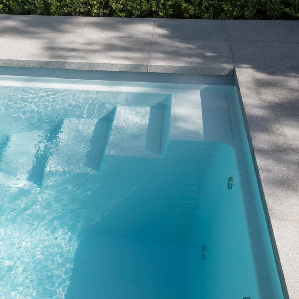 Ein leeres Schwimmbecken mit klarblauem Wasser und Stufen, umgeben von grauen Fliesen.