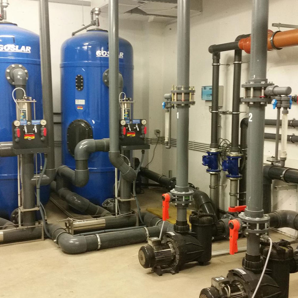 Industrieanlagenraum mit blauen Tanks, grauen Rohren und Ventilen.