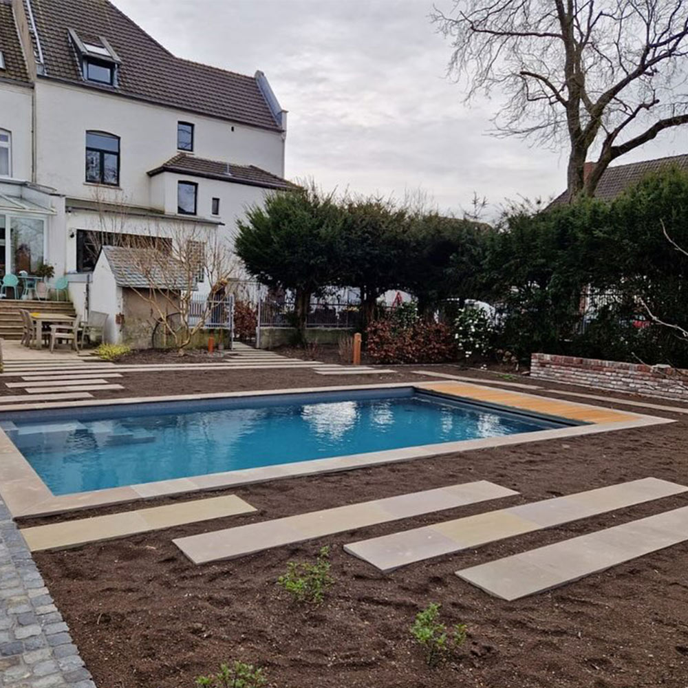 Garten mit einem rechteckigen blauen Pool, umgeben von einigen Pflastersteinen und kahlen Bäumen.